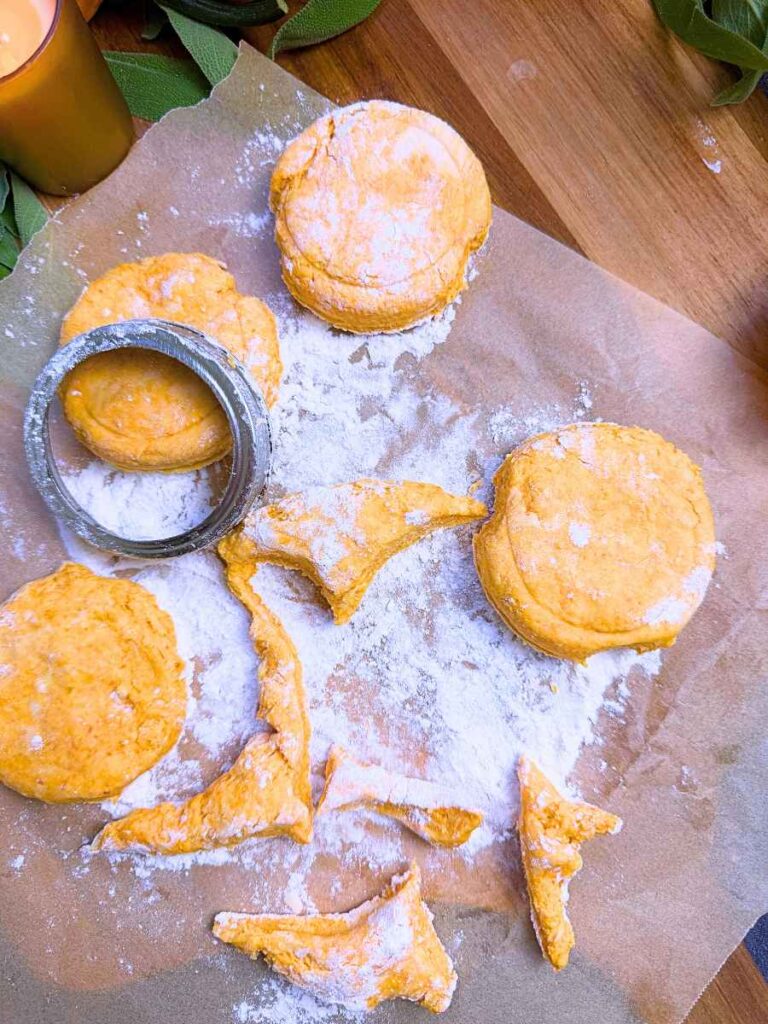 Round unbaked pumpkin biscuit dough on a piece of parchment paper. There is a canning jar ring on top of one.