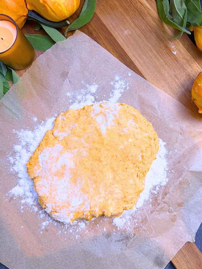 Pumpkin biscuit batter pressed into a flat round shape on a piece of parchment paper.