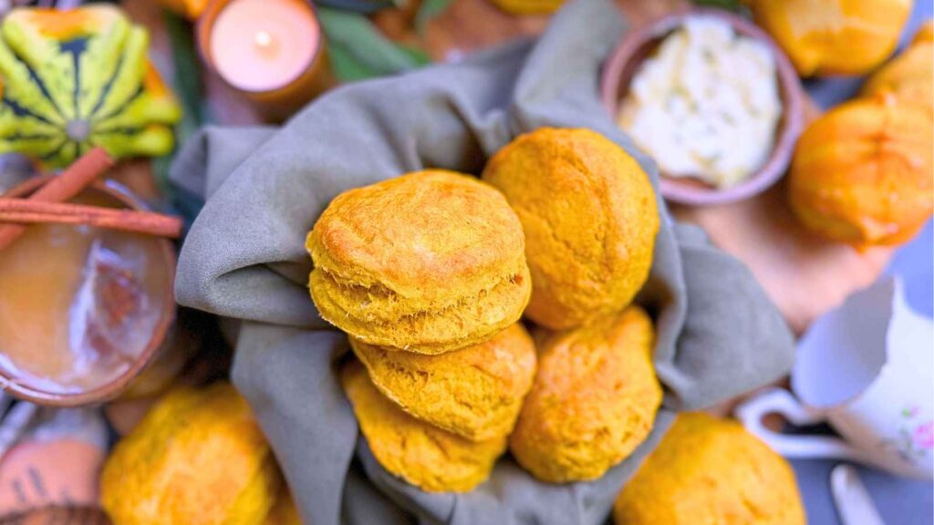 A basket of pumpkin biscuits. There are some off to the side and a small wooden bowl with butter.