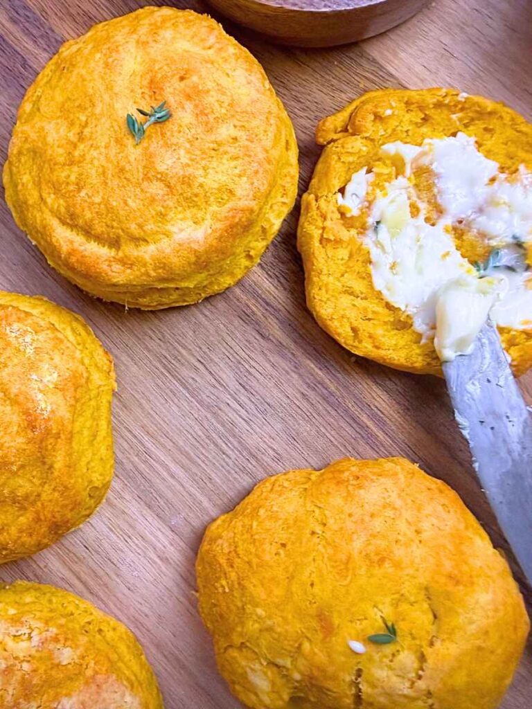 Pumpkin biscuits on a wooden board. One is split in half and buttered.