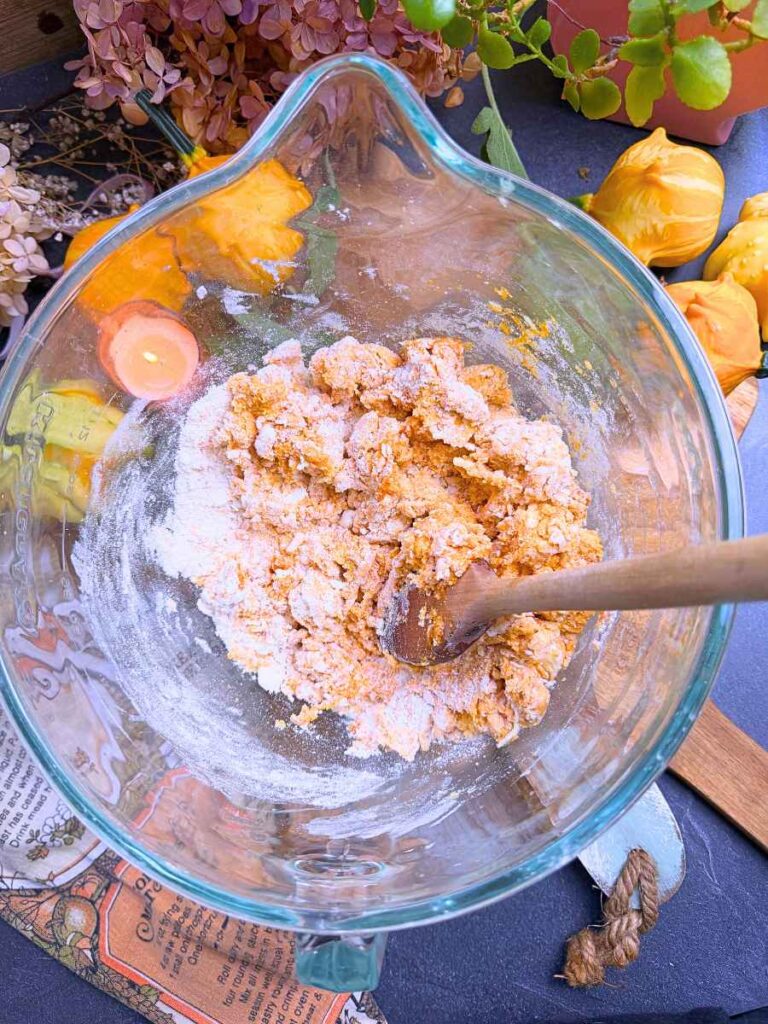 A large glass bowl with pumpkin biscuit batter and a wooden spoon inside.