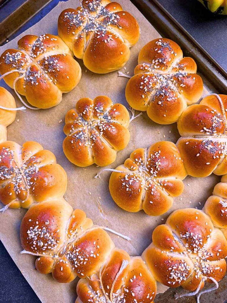 Baked pumpkin shaped dinner rolls on a lined baking sheet.