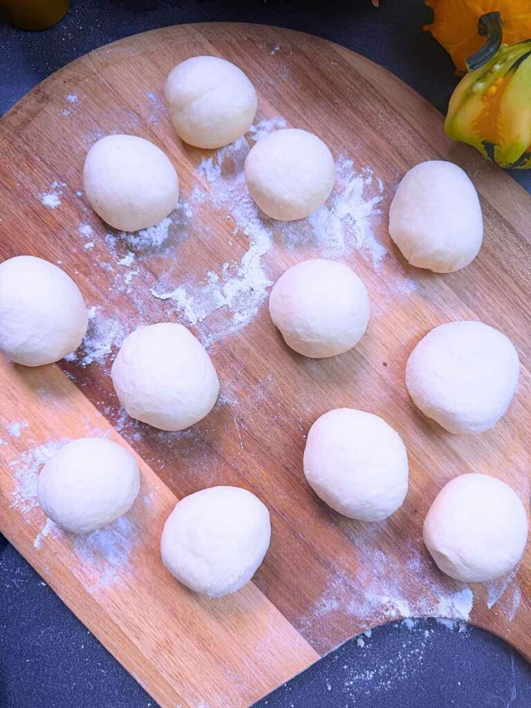 Twelve shaped dough dinner rolls on a pizza peel.