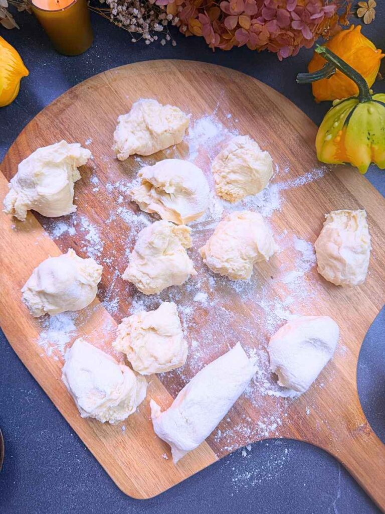 A collection of small portions of bread dough on a pizza peel.