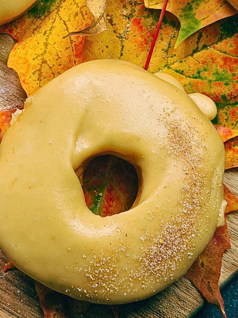 A caramel dipped baked pumpkin doughnut on a table of maple leaves.