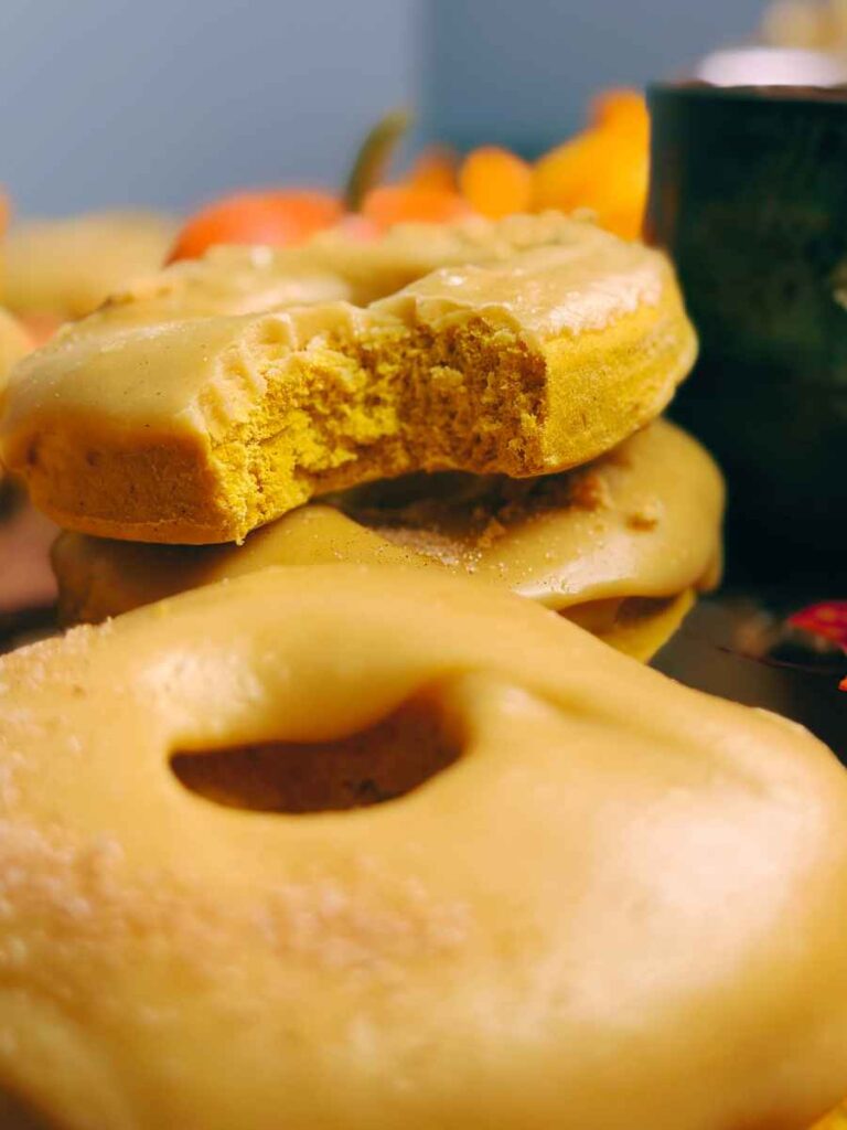 A pumpkin doughnut with a bite out of it. There is one in front.