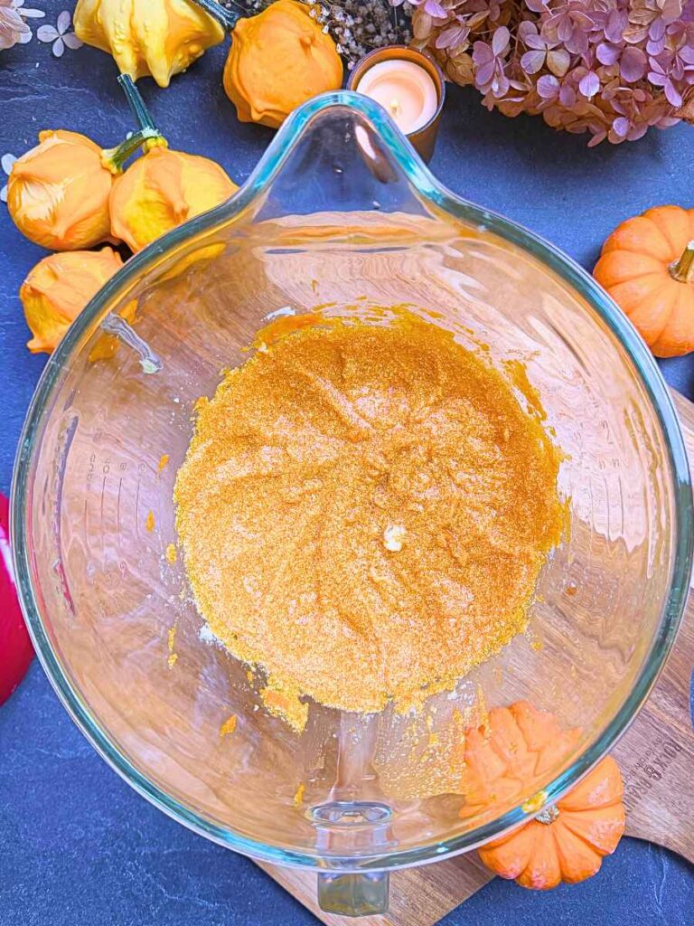 Creamed butter, sugar, eggs, and pumpkin in a large glass bowl.