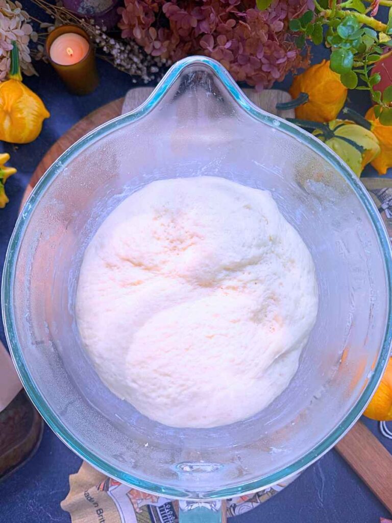 Risen bread dough in a glass bowl.