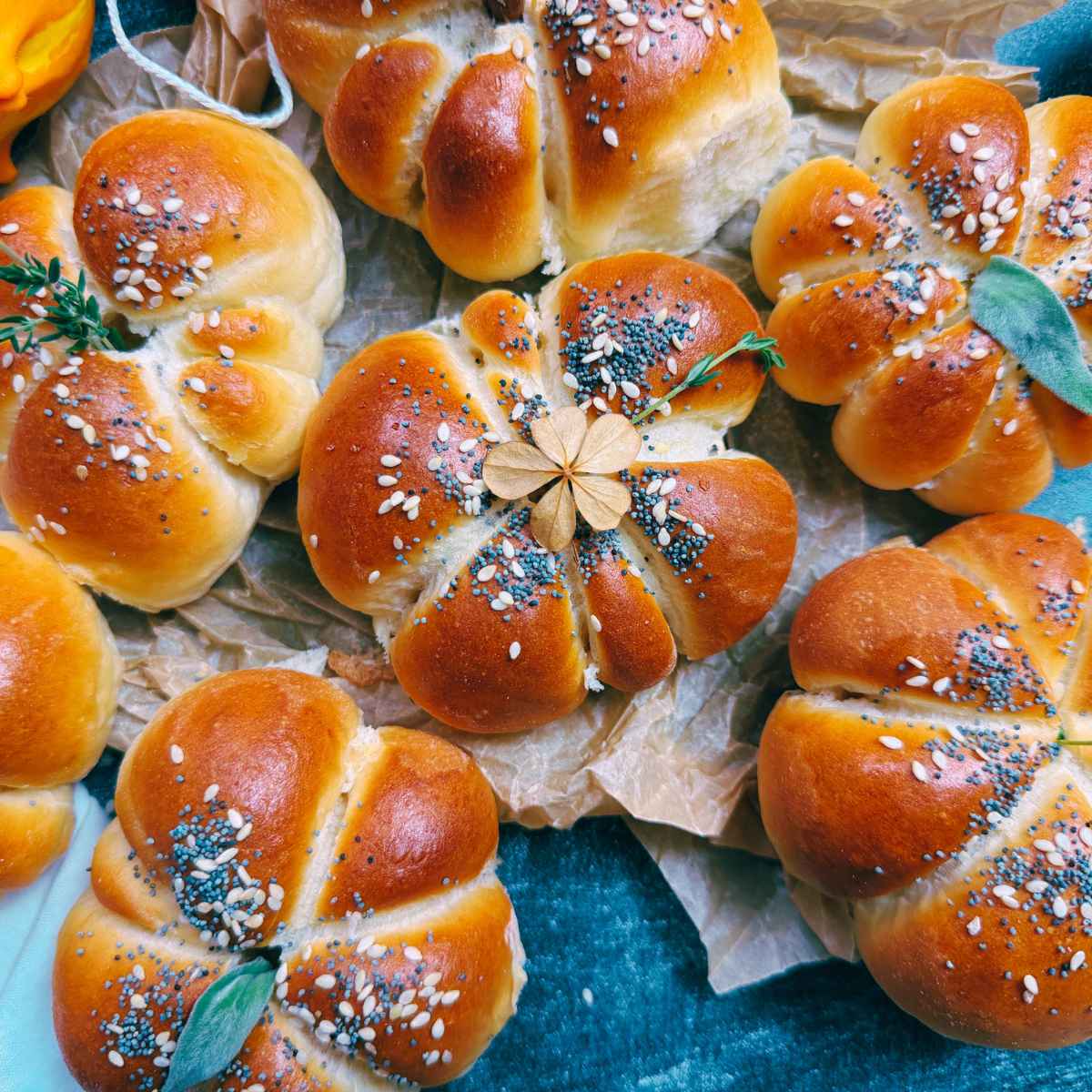 A collection of pumpkin shaped dinner rolls garnished with poppy and sesame seeds and fresh herbs.