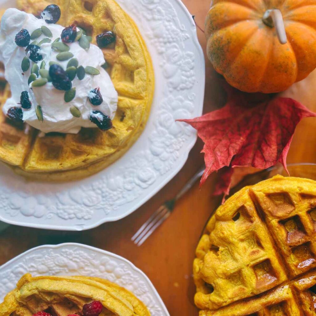 Three stacks of waffles. One is toped with whipped cream, pumpkin seeds, and dried cranberries.