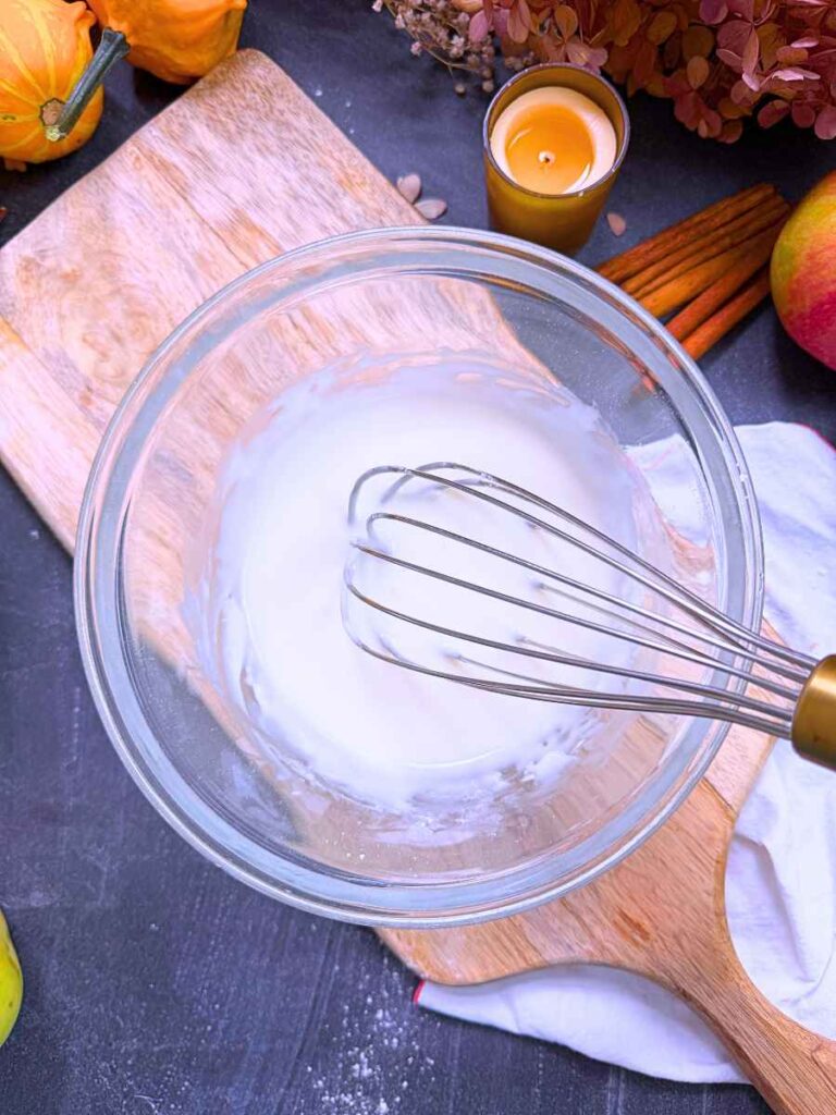 A woman is mixing a vanilla glaze with a whisk.