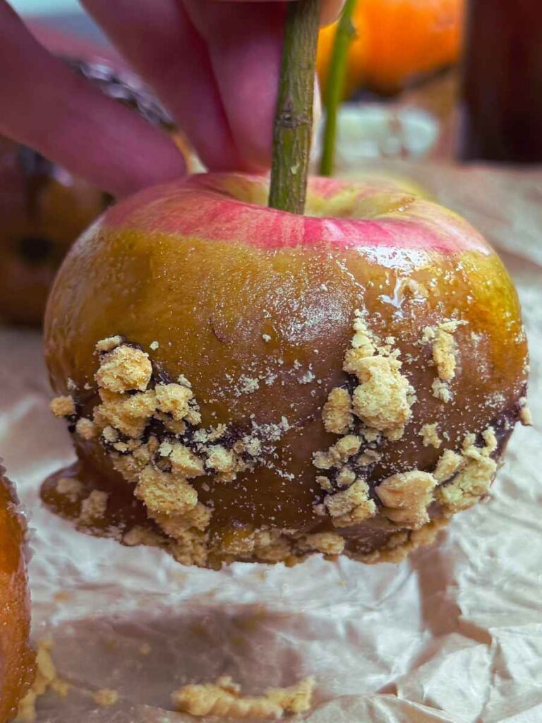 A maple dipped candy apple with crushed cookie crumbs.