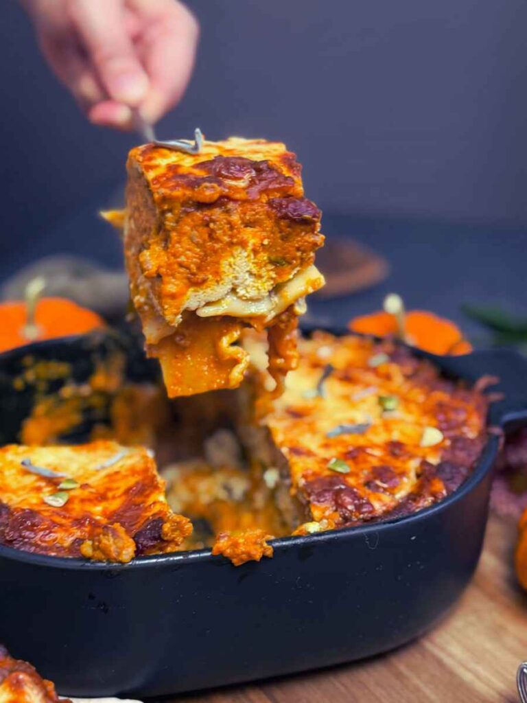 A woman is holding a portion of pumpkin lasagna on a metal spatula.