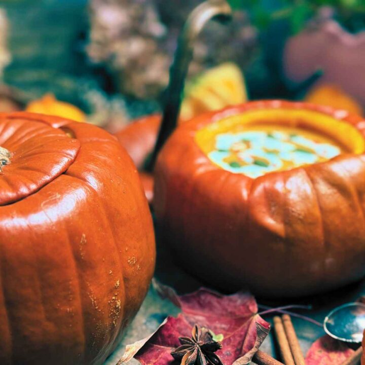 Two cooked pumpkins. One has the top on and the other is filled with pumpkin soup.