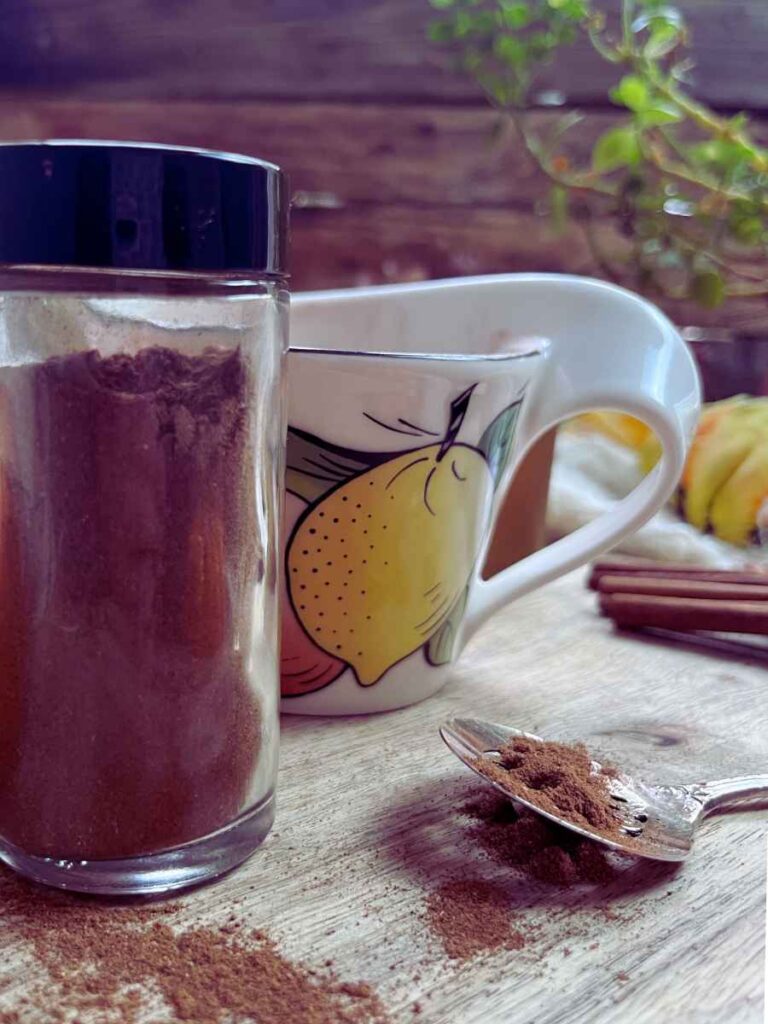 A small glass jar of pumpkin spice, There is a mug in the background.