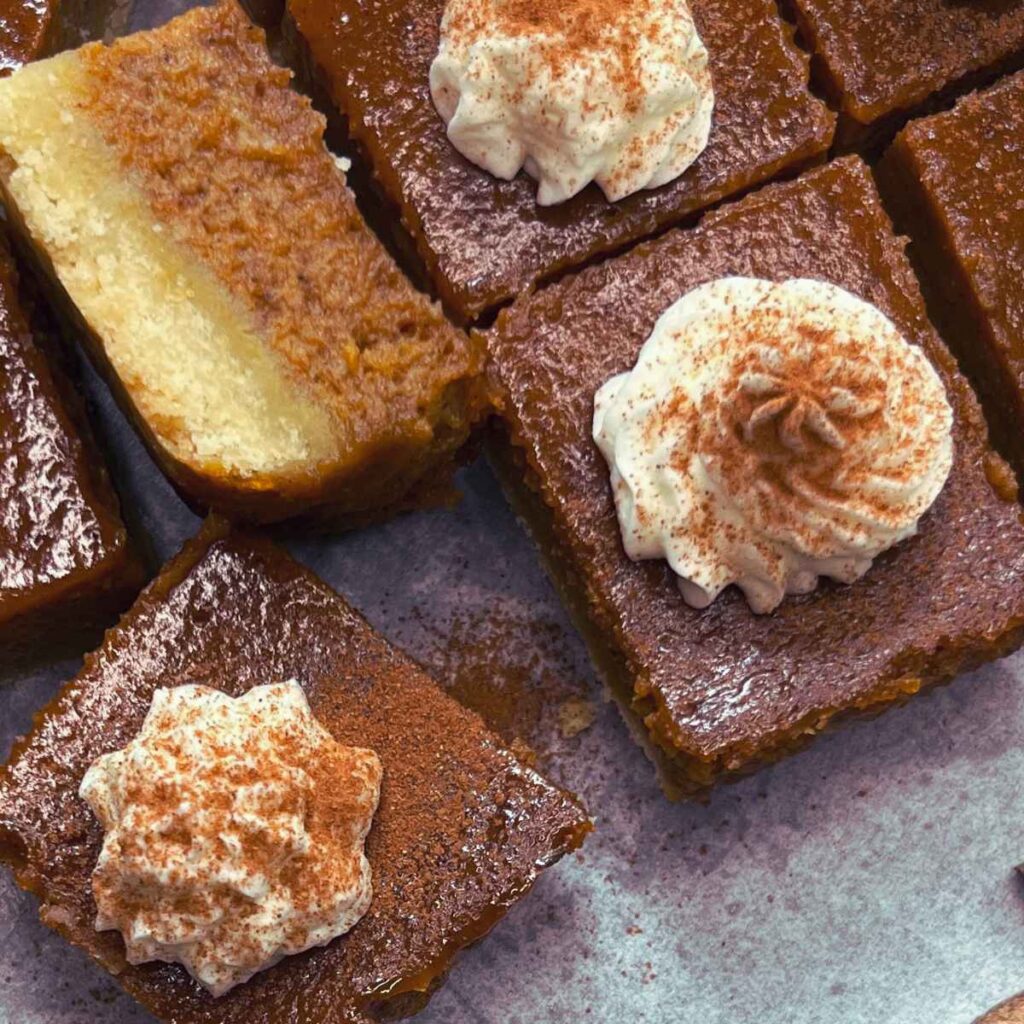 Pumpkin pie bars decorated with whipped cream and pumpkin pie spice.