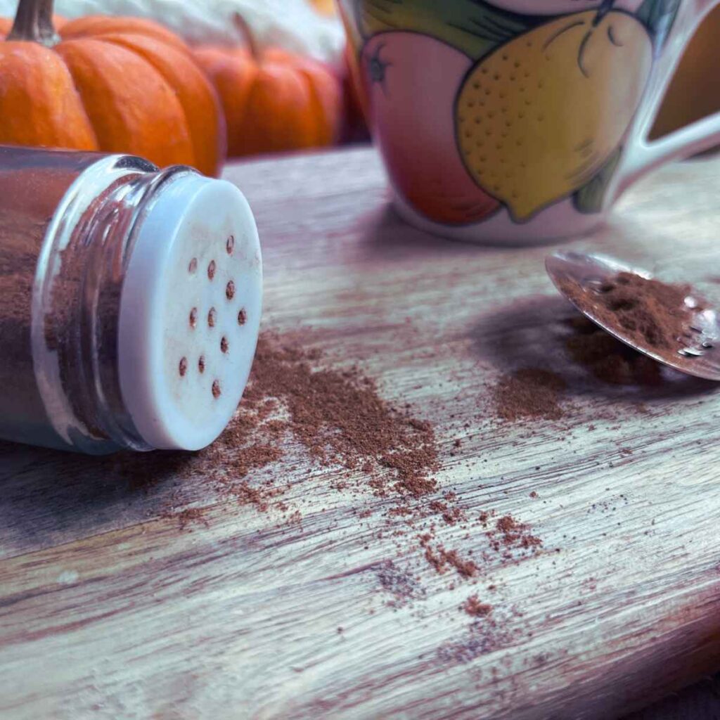A tipped over spice jar with pumpkin pie spice inside. There is a mug in the background.