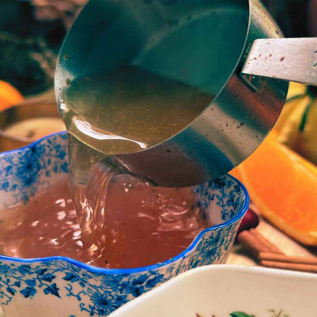 A woman is pouring mulled apple cider into a blue floral mug.