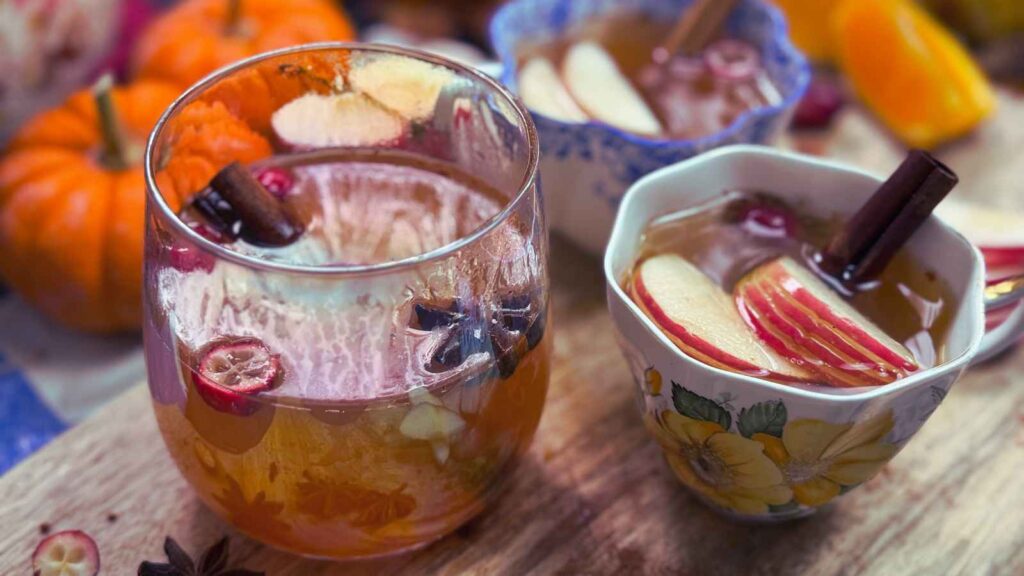 Two cups of spiced apple cider. There is sliced apples, cinnamon sticks and anise in the mugs.