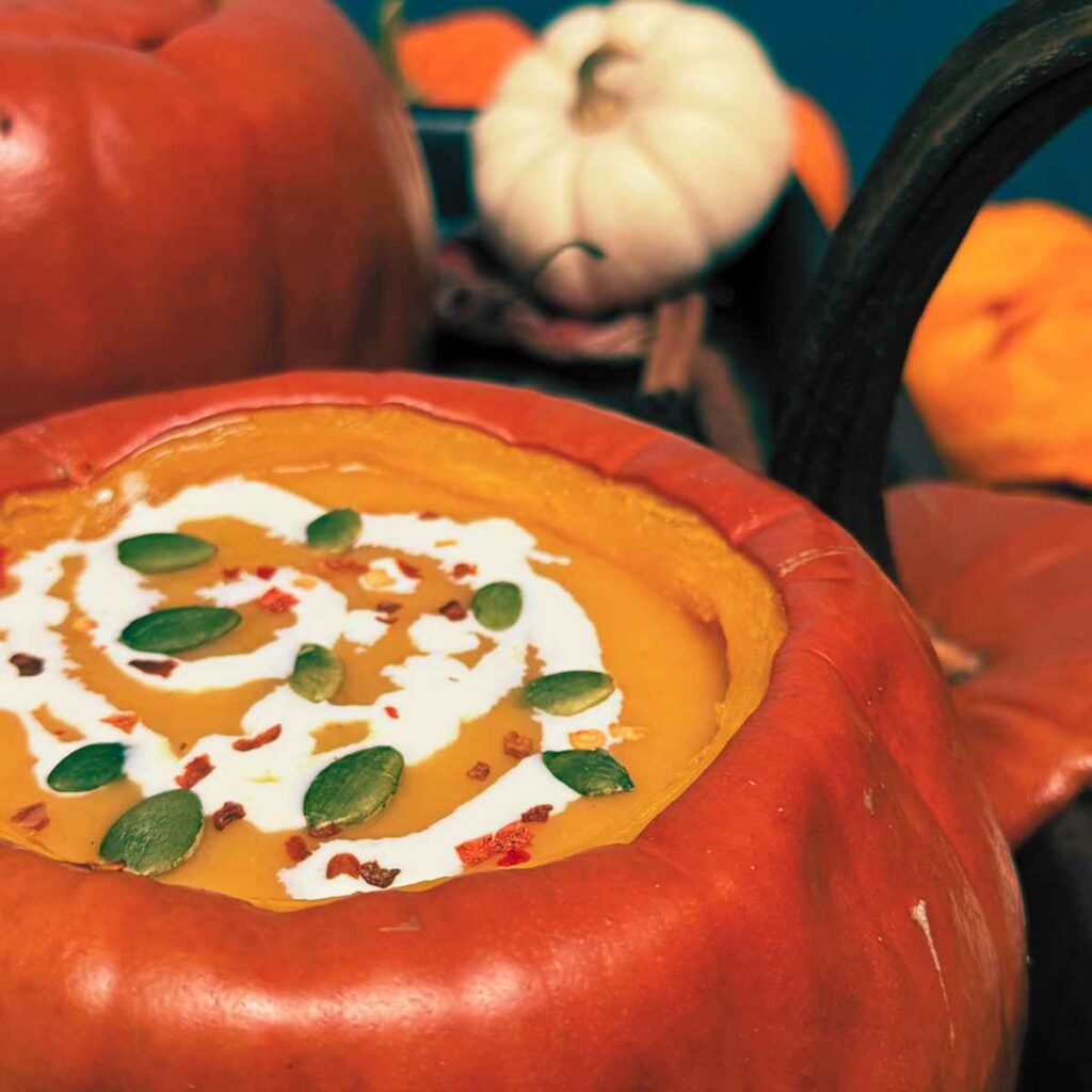 Pumpkin soup inside of a cooked pumpkin. There are more pumpkins in the background.