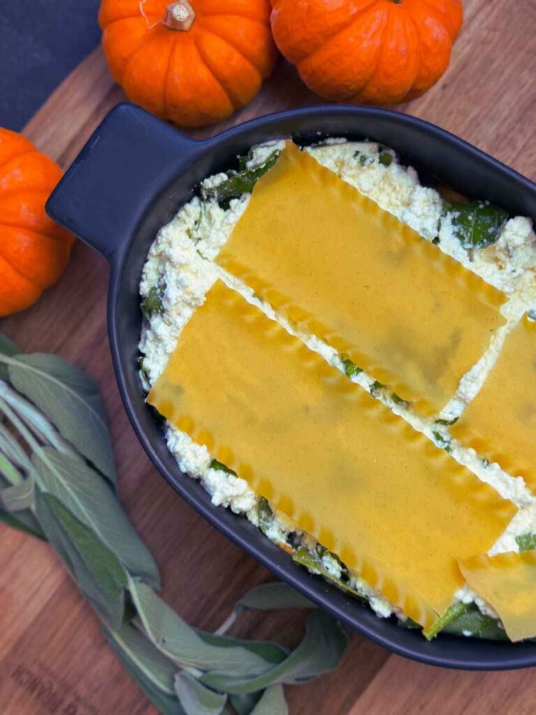 A black casserole dish with ricotta cheese and spinach covered by lasagna noodles.