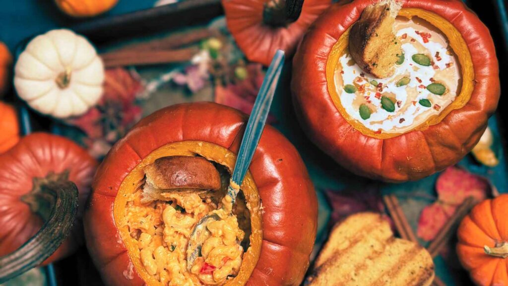 Two cooked pumpkin bowls. One has soup in it and one has pasta in it.