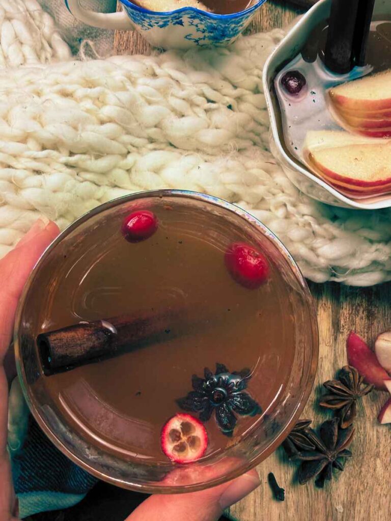 A woman is holding a glass of mulled apple cider.